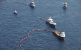 Ships in the ocean with floating barriers, conducting an oil spill cleanup.