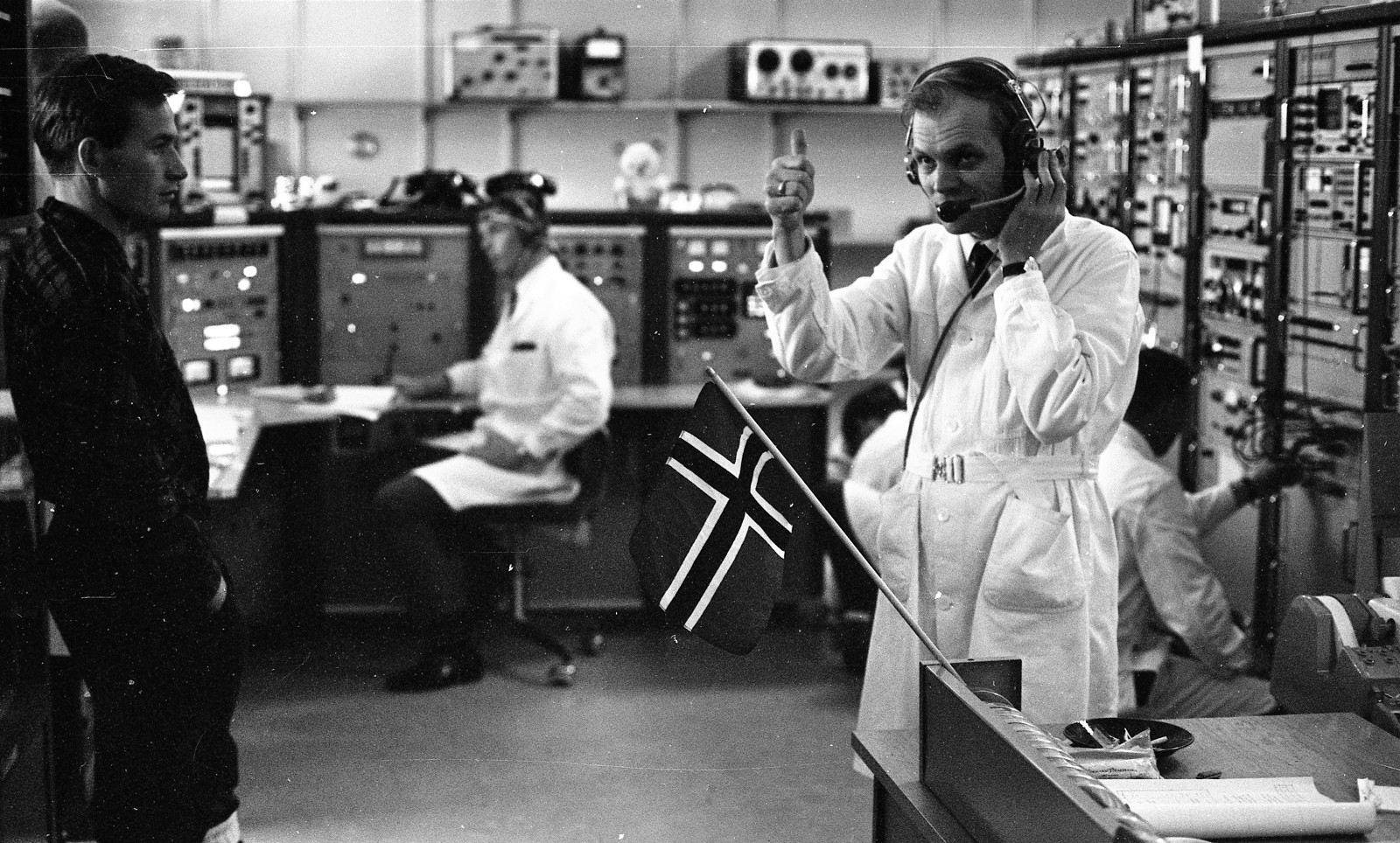 Scientists in a control room with a Norwegian flag, operating equipment and communicating.