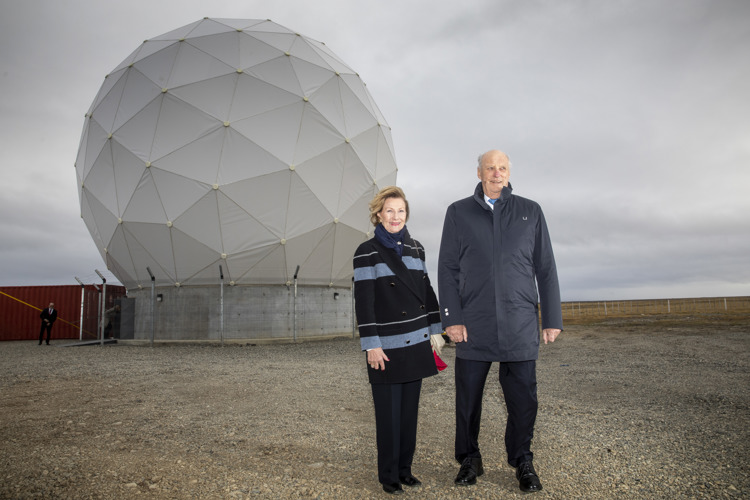 A man and a woman standing in front of a large geodesic dome structure outdoors, both wearing dark coats.
