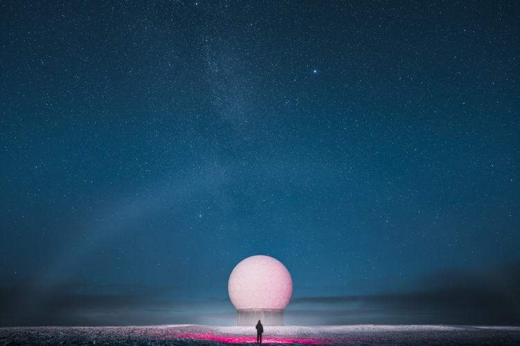 A person standing in front of a large geodesic dome under a starry night sky.