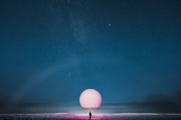 A person standing in front of a large geodesic dome under a starry night sky.