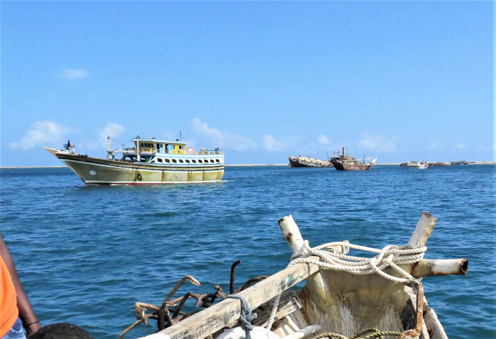 Several boats on calm blue waters under a clear sky, with one boat in the foreground and others in the distance.