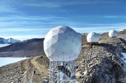 Multiple geodesic dome antennas on a rocky landscape with mountains and a clear sky in the background.