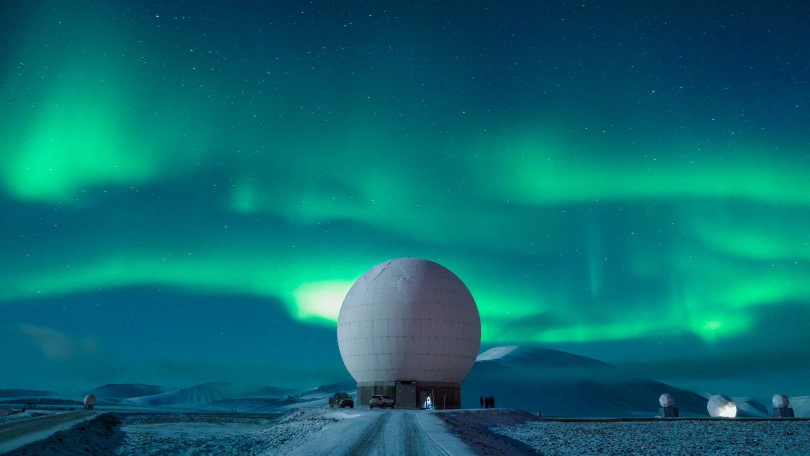 Large white spherical radar dome against a backdrop of the northern lights and starry night sky.