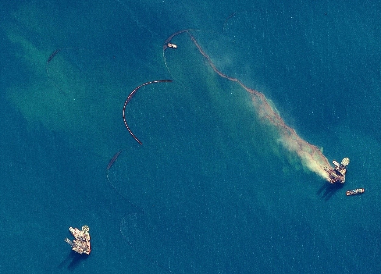 Aerial view of an offshore oil spill with visible containment efforts and boats in the surrounding water.
