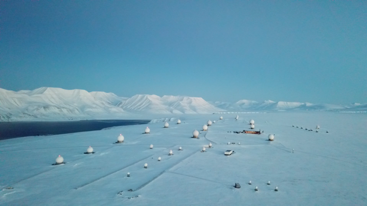 Snow-covered satellite station with multiple domes, set against a backdrop of icy mountains and a clear blue sky.