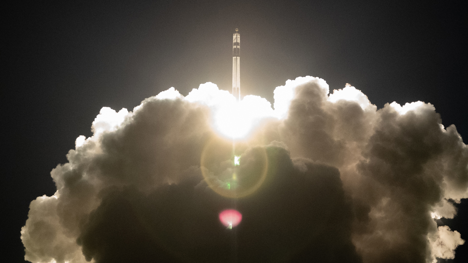 Rocket ascending into the sky, surrounded by bright flames and thick clouds of smoke, against a dark background.