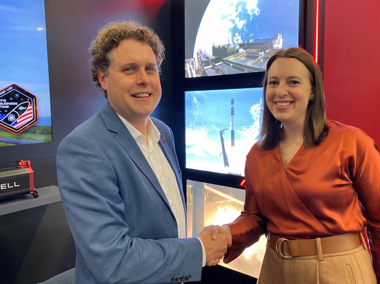 Two people shaking hands in front of screens displaying space-related images, smiling at the camera.