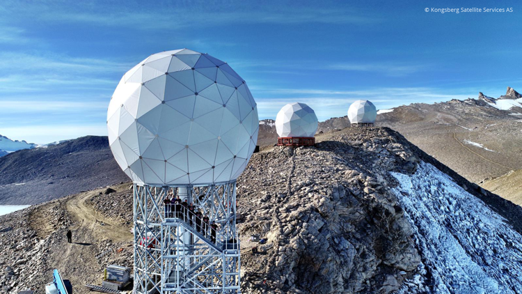 Geodesic domes on mountain peaks, part of a satellite station, with a clear blue sky and rocky terrain.